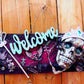 Welcome Sign With a Silver Colored Skull With  Piercings Wearing a Crown And Her Scepter