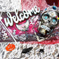 Welcome Sign With a Silver Colored Skull With  Piercings Wearing a Crown And Her Scepter